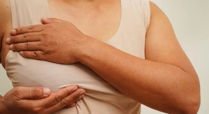 Close-up of a person lifting their light sleeveless shirt to inspect the chest/underarm area with both hands visible.