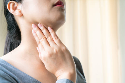 close-up of a person pressing their throat with fingers, indicating throat pain or discomfort.