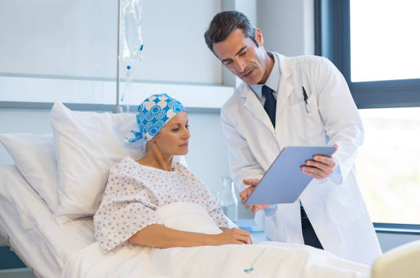 doctor shows a tablet to a patient in a hospital bed, discussing care plan with iv in view.